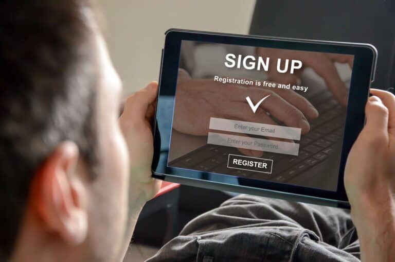 Photo of the a man holding a tablet computer with a "Sign Up - Registration is free and easy" on the screen