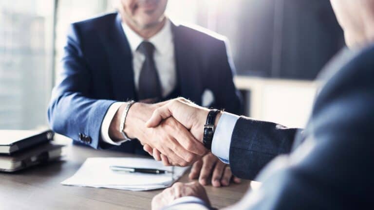 Photo of two businessmen in suits shaking hands across a table