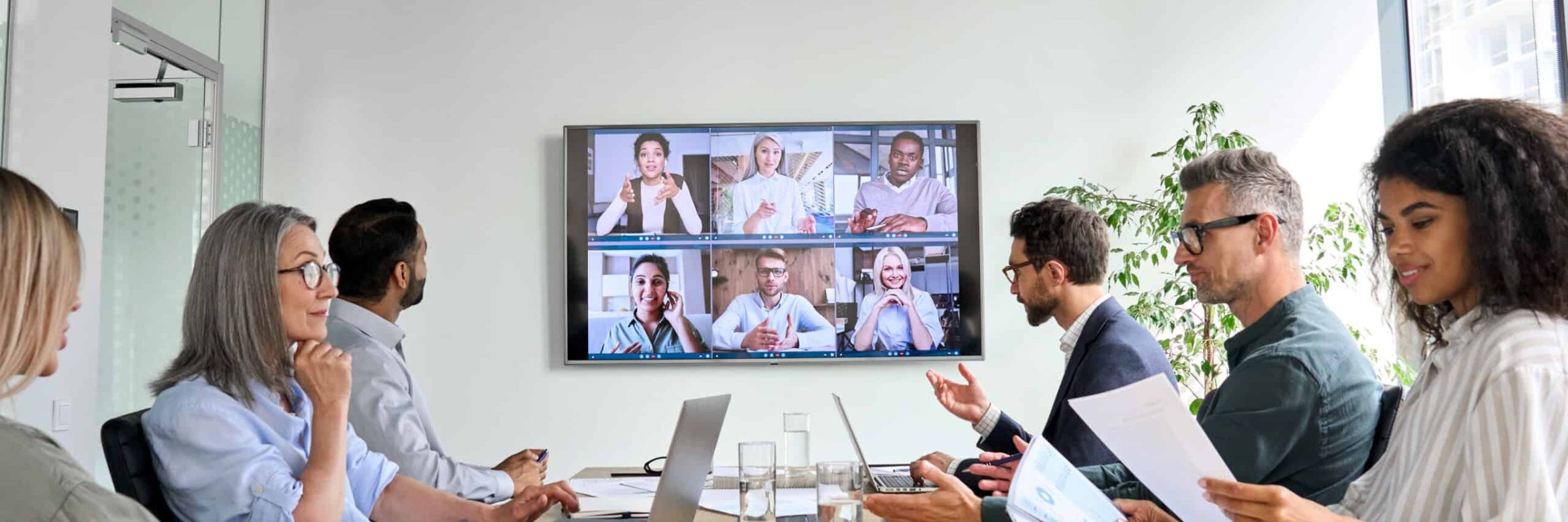 Diverse employees having online conference video call on tv screen monitor in board meeting room